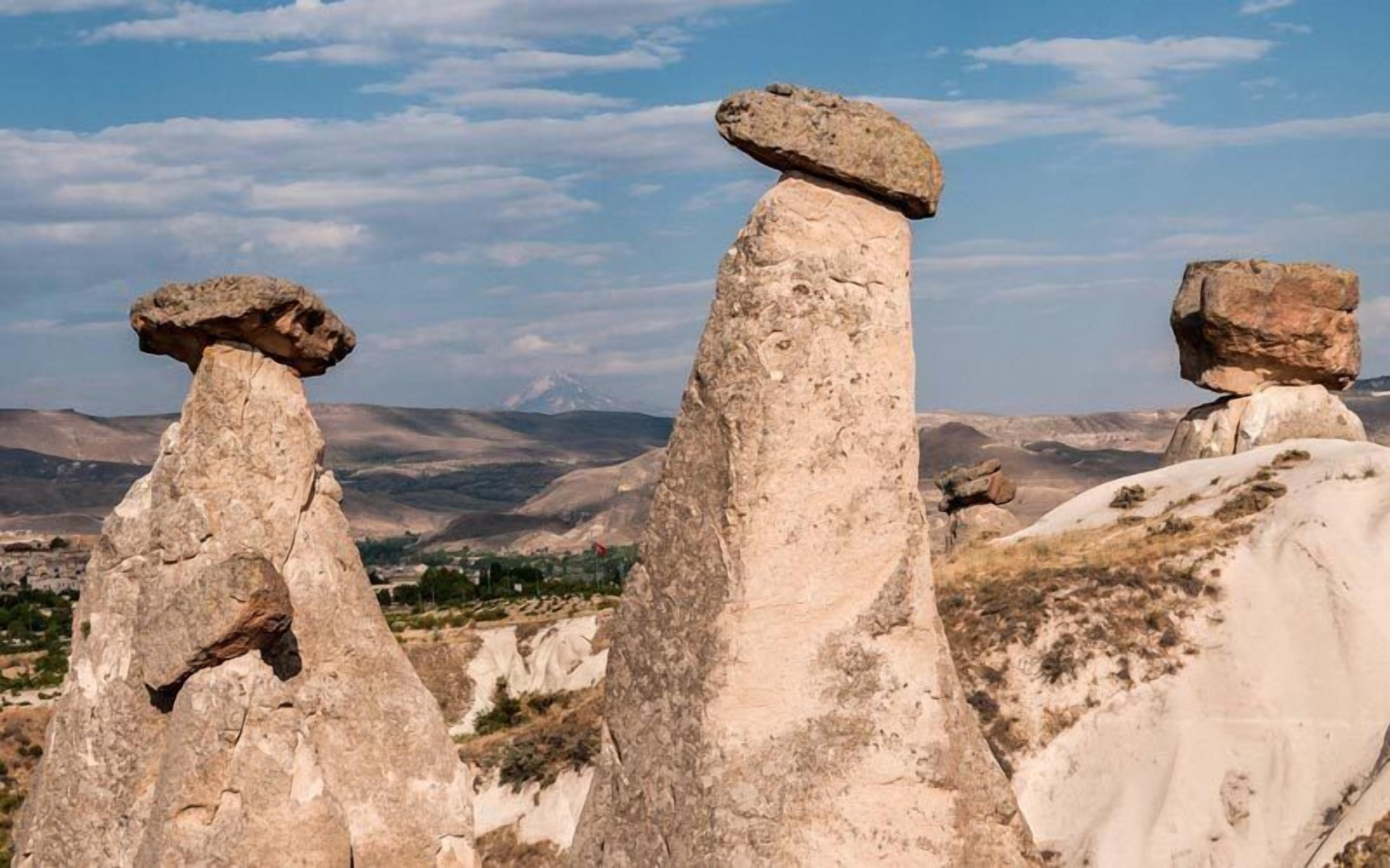 Des formations rocheuses se dressent sous un ciel dégagé, avec des montagnes qui se profilent à l'horizon.