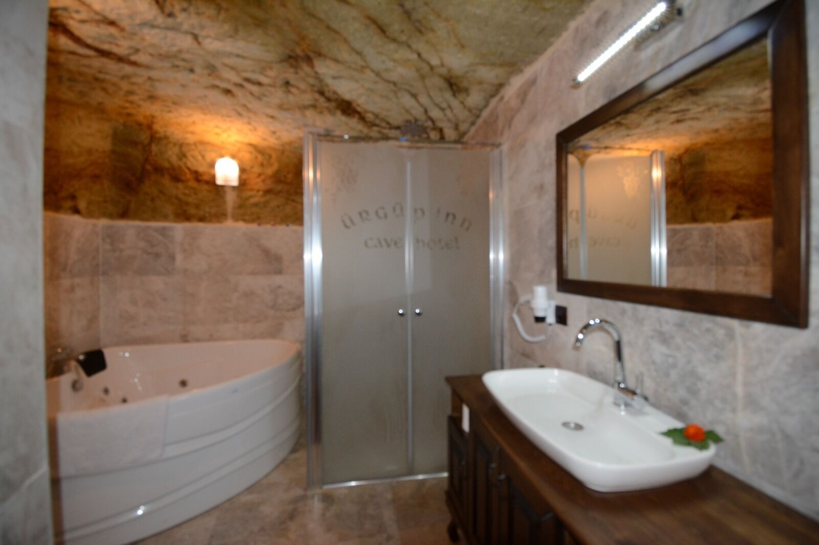 A bathroom with a marble wall, a bathtub, a sink, and a mirror.