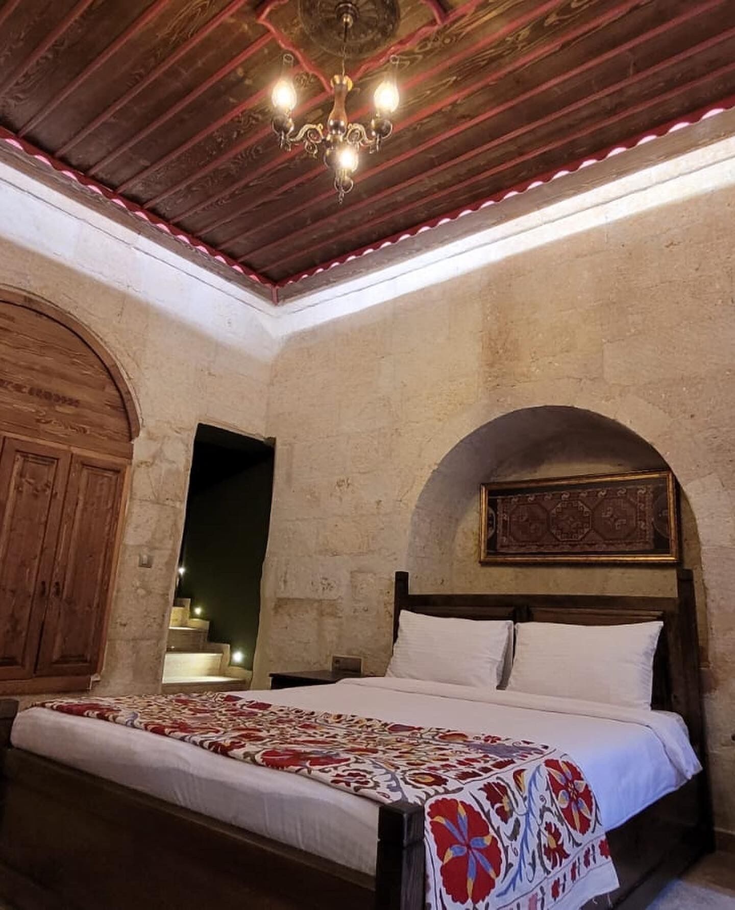 A bedroom with a wooden bed, a chandelier, and a stone wall.