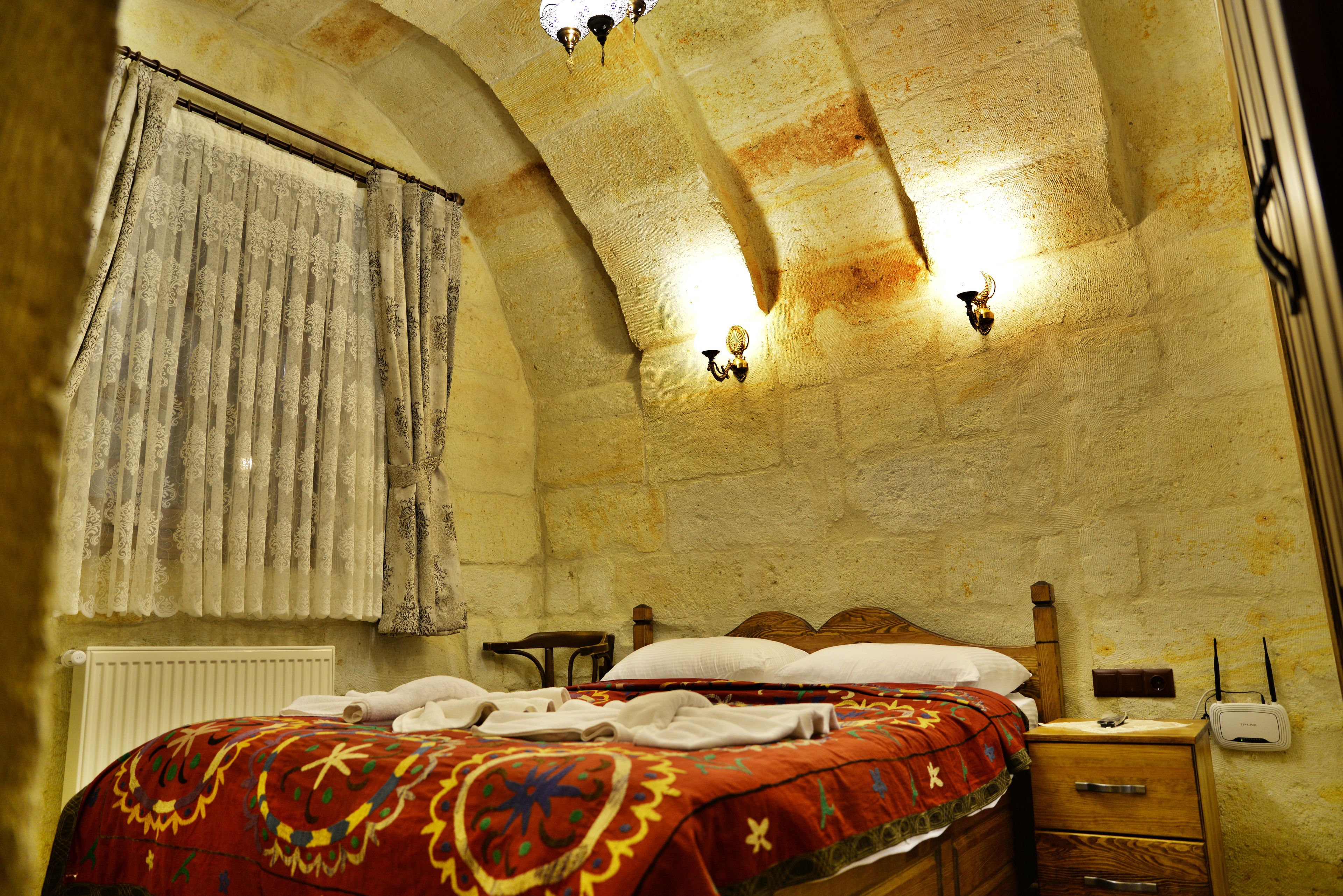 A room with a bed, a wooden nightstand, a radiator, and a wall-mounted light fixture.