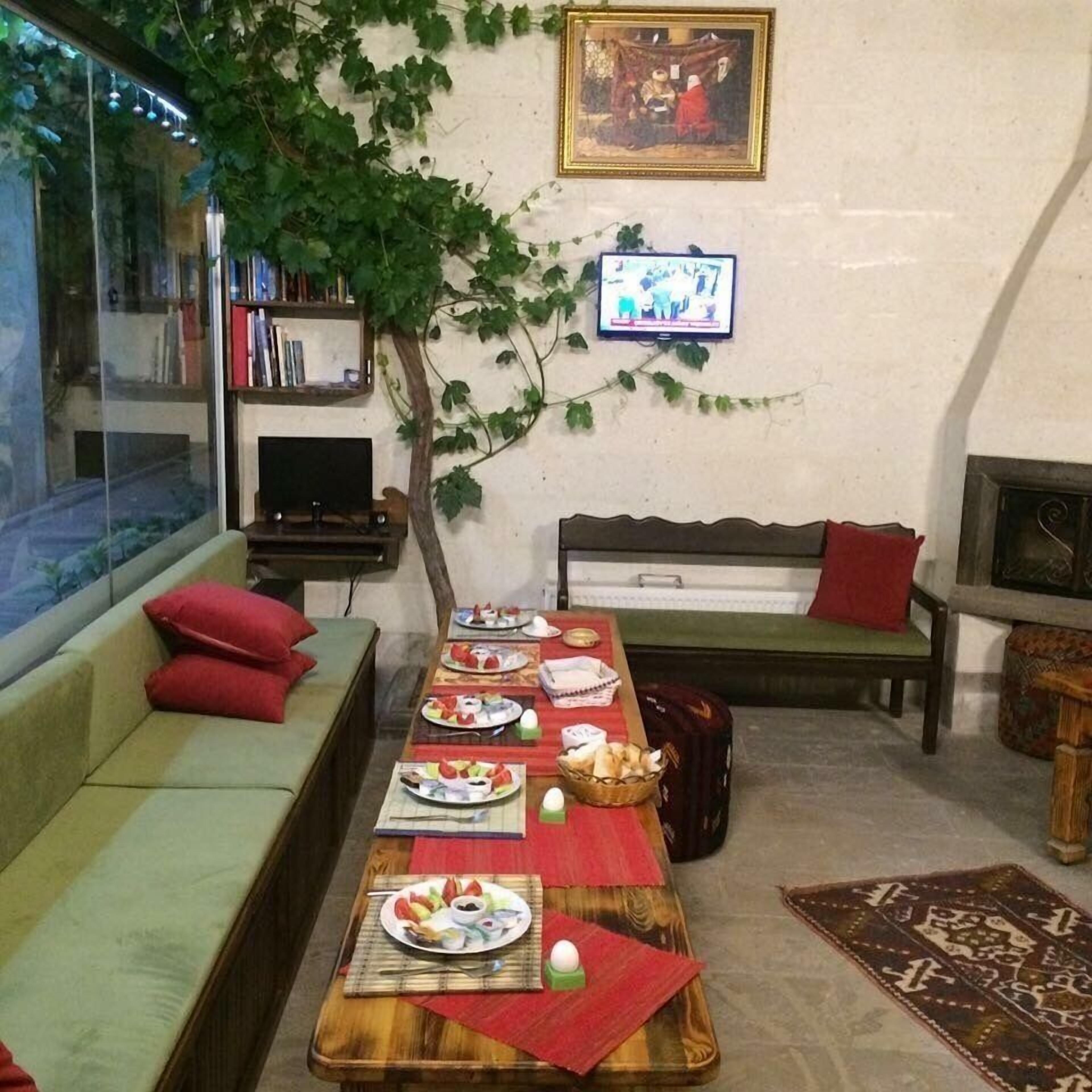 A cozy living room with a long wooden table set for a meal, a green sofa, a wooden bench, and a TV mounted on the wall.