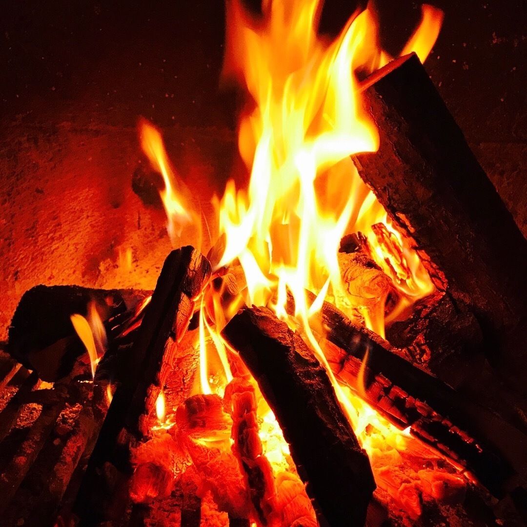 A close-up of burning wood, likely a fireplace, with flames consuming the logs.