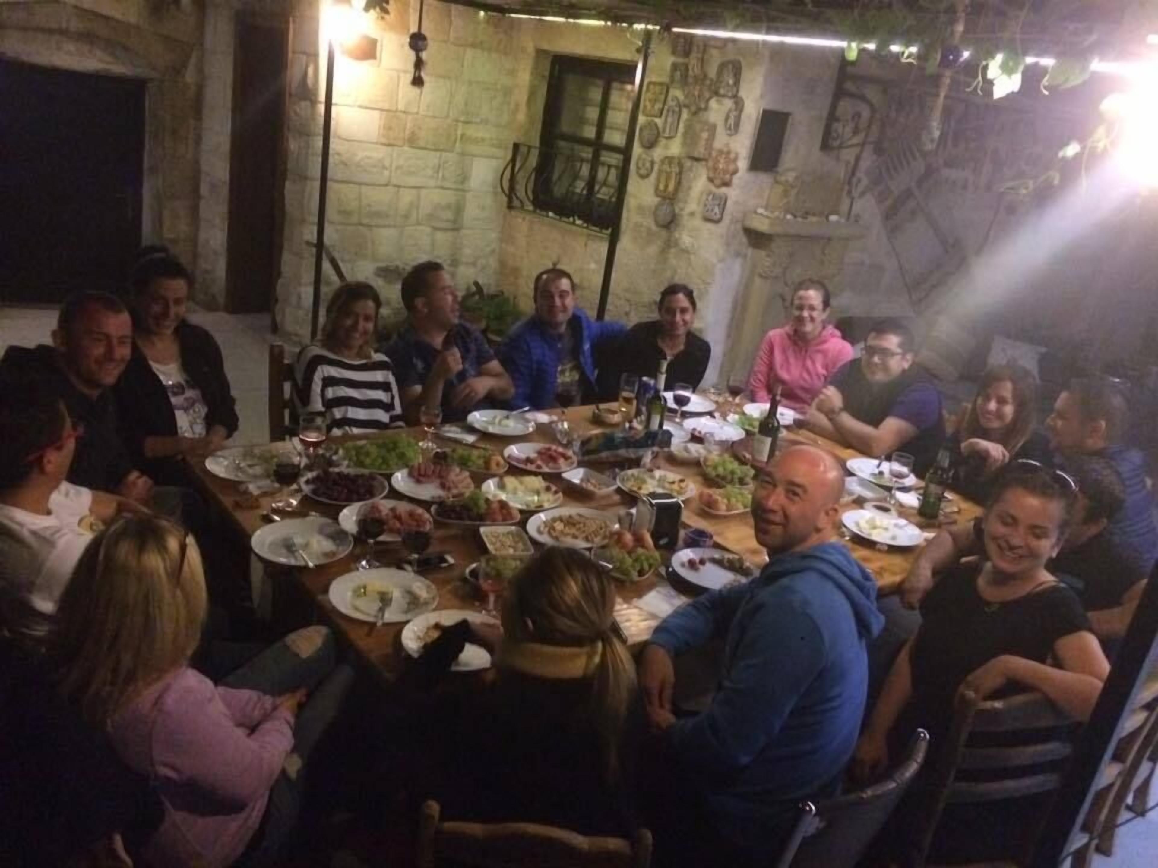 A group of people seated around a table with various dishes and drinks, in a room with stone walls and a window.