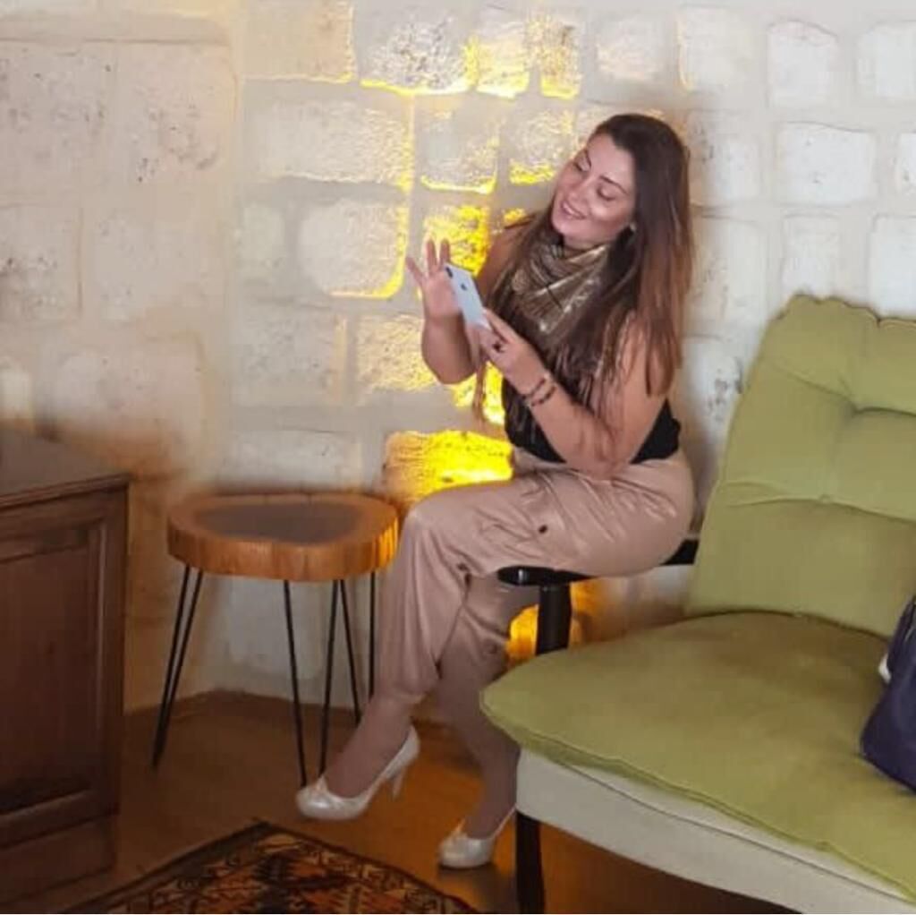Eine Person sitzt auf einem grünen Sofa in einem Zimmer mit einer Steinwand und einem kleinen Holztisch.