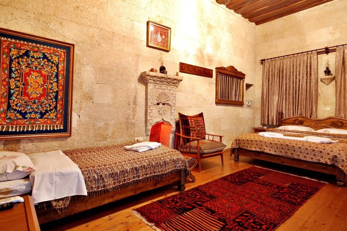 A traditional room with two single beds, a wooden chair, a patterned rug, and a stone fireplace.