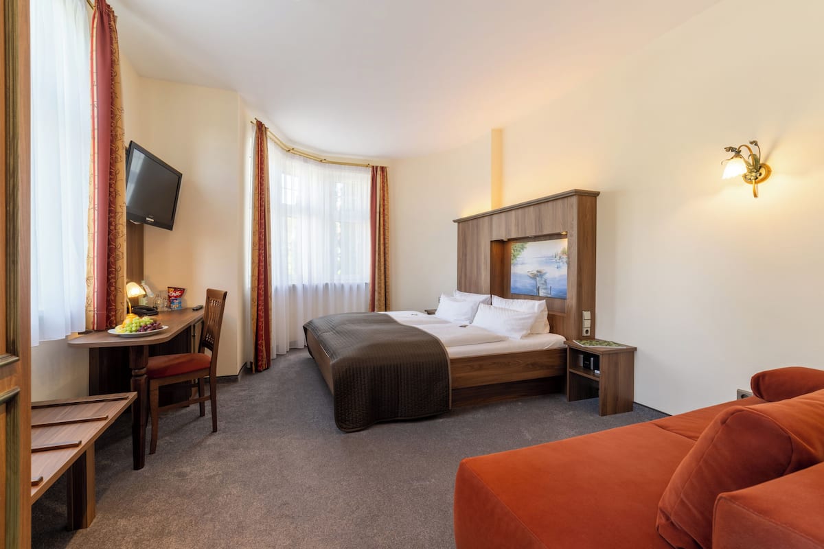 Ett hotellrum med en säng, ett skrivbord med en stol, en tv och en tavla på väggen.