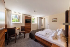 Habitación de hotel con cama, escritorio, dos sillas, televisión y ventana con vistas a zonas verdes.