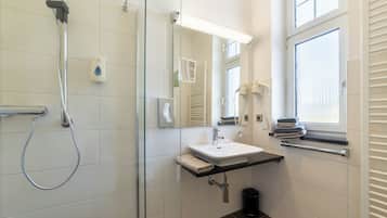 A modern bathroom with a glass shower enclosure, a white sink, a mirror, and a window.