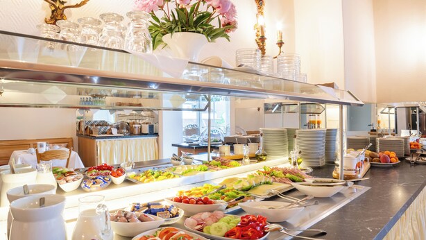 A buffet with various food items and a decorative vase of flowers. - Schöngarten Garni (Lindau)