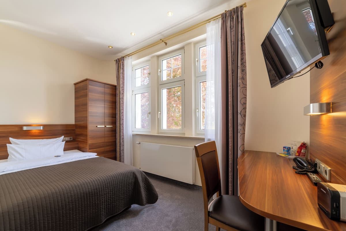 Ett hotellrum med en säng, ett skrivbord, en stol, en tv och ett fönster med gardiner.