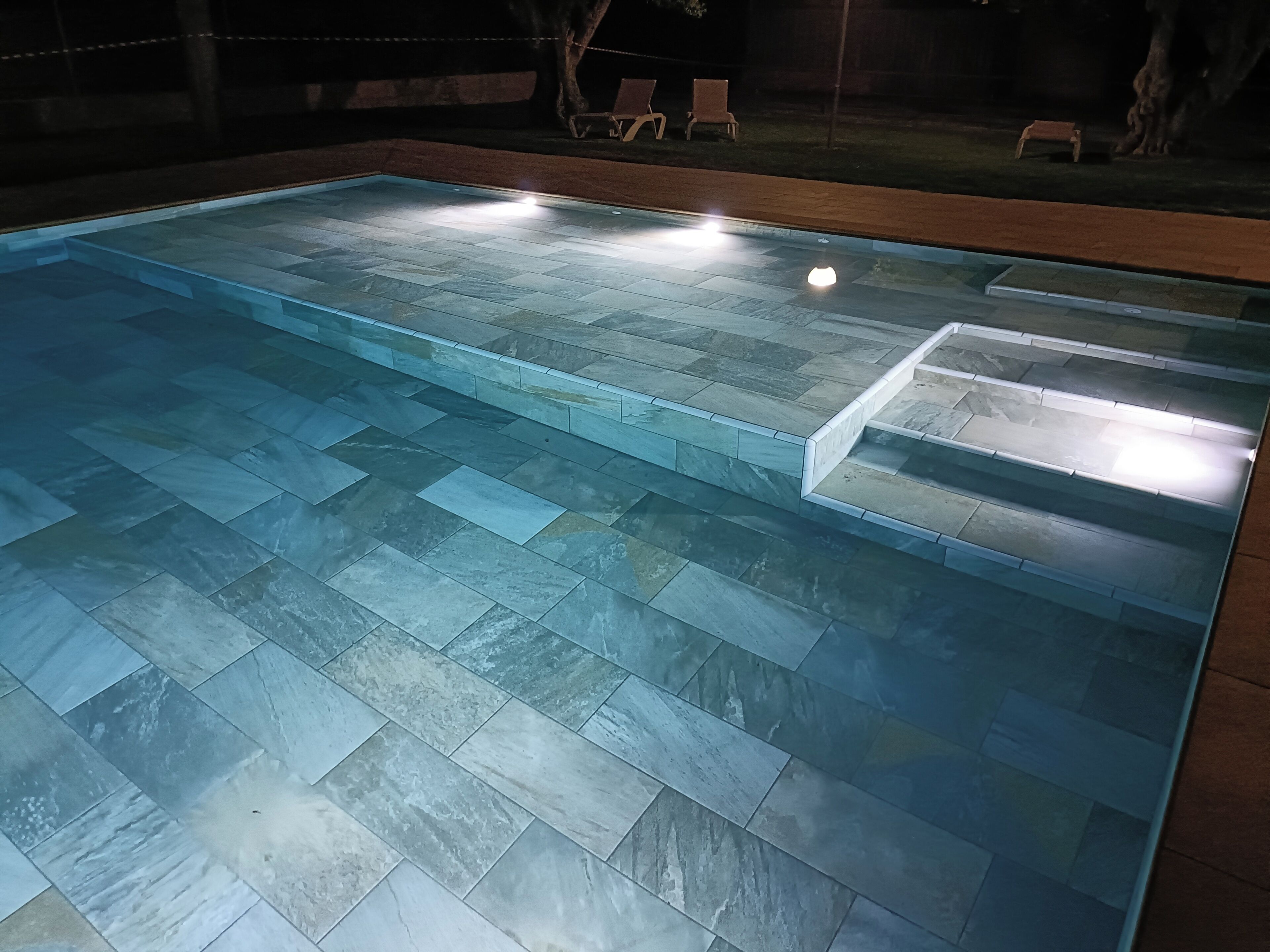 Una piscina amb solàrium de rajola i escales que baixen a l'aigua.