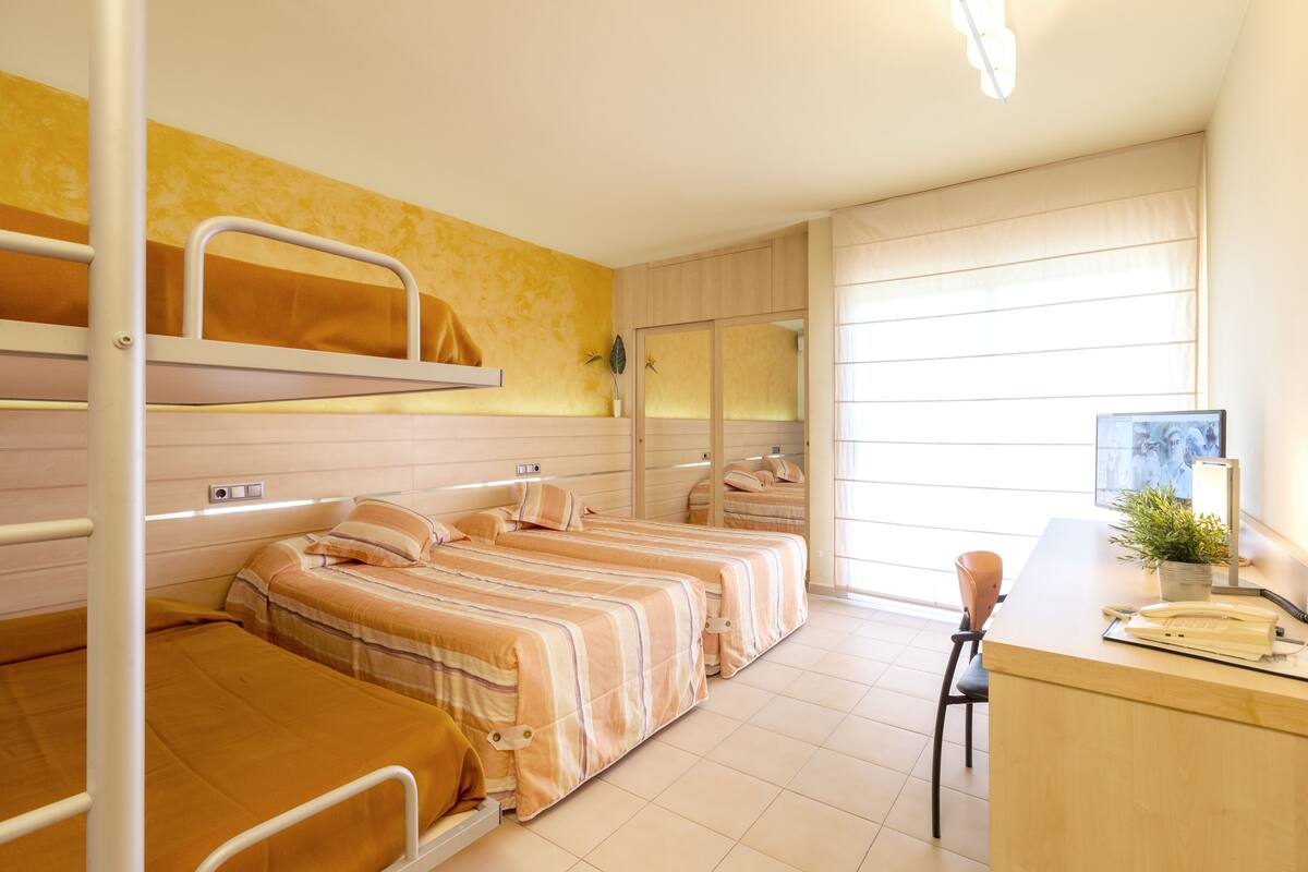 Ein Schlafsaalzimmer mit Etagenbetten, einem Schreibtisch und einem Fenster mit Jalousien.