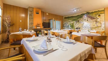 Um restaurante com várias mesas preparadas para refeições, uma televisão ao fundo e um mural na parede.