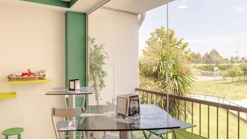 Un balcón con una mesa de vidrio, sillas y vistas a zonas verdes y una carretera.