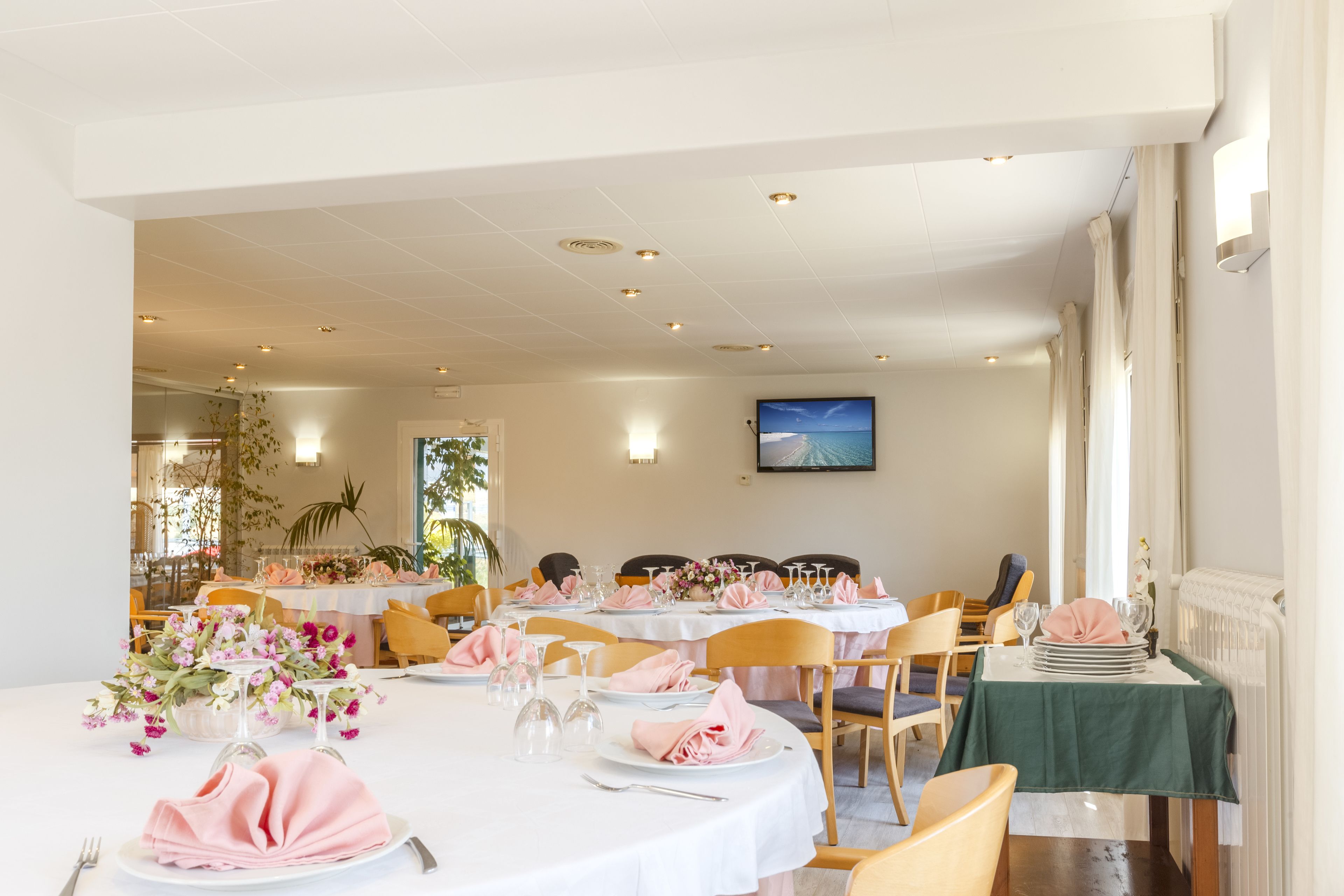 A dining area with round tables, chairs, and neatly set tables with pink napkins and white tablecloths.