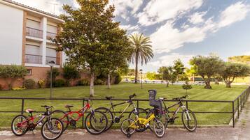 Una fila de bicicletas estacionadas junto a un edificio con un área verde y árboles al fondo.