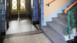 A hallway with a double door, a staircase with green railings, and tiled walls. - Apartmenthaus Stadt Metz (Dresden)