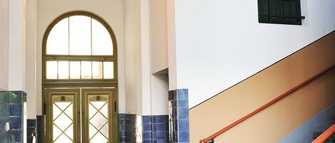 Ein Flur mit einer Doppeltür, einer Treppe mit grünen Geländern und gefliesten Wänden.