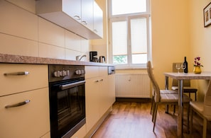 A kitchen with white cabinets, a black oven, a coffee maker, and a dining table with chairs. - Apartmenthaus Stadt Metz (Dresden)