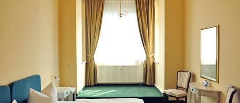 Une chambre d’hôtel avec un lit, une chaise, une petite table, un miroir et une vue sur l’extérieur grâce à de grandes rideaux.