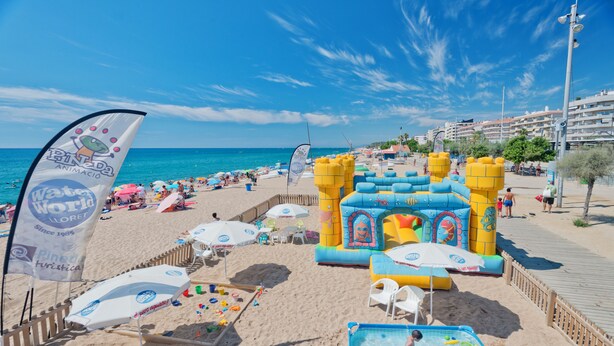 A beach with inflatable play structures, umbrellas, and a pool area. - Hotel Sabiote (Pineda de Mar)
