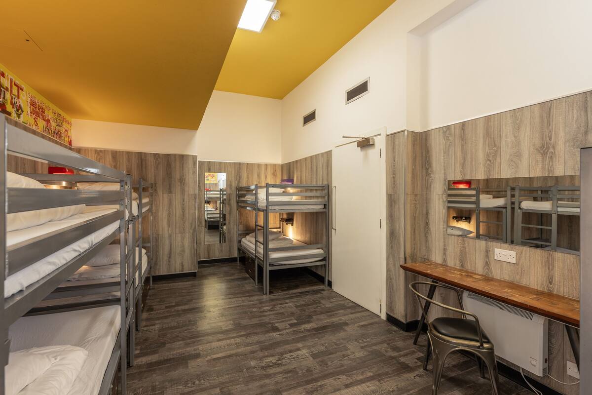 A bunk room with wooden flooring, bunk beds, a desk, and a chair.