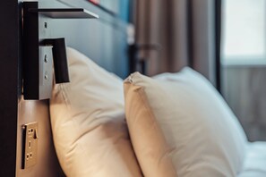 A bed with beige pillows and a black headboard, a power outlet, and a switch on the wall. - Kabannas Newcastle (Newcastle-upon-Tyne)