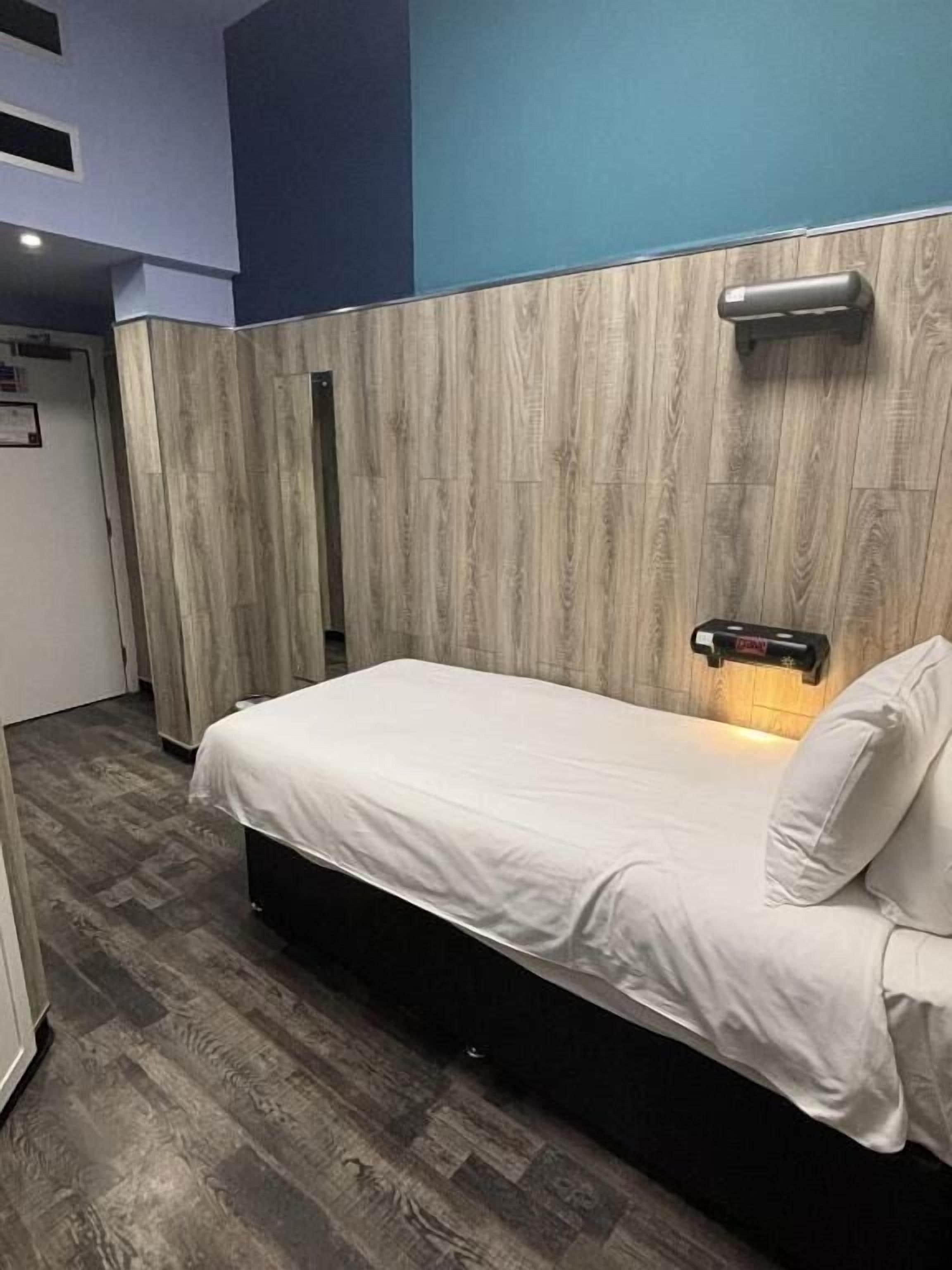 A single bed with a headboard, a wooden wall panel, and a small bedside table with a lamp.