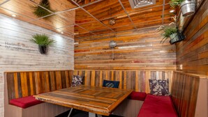 A wooden-paneled room with a central table, red cushioned seating, and hanging plants.