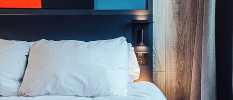 A neatly made bed with white linens, a bedside table with a lamp, and a wooden headboard.