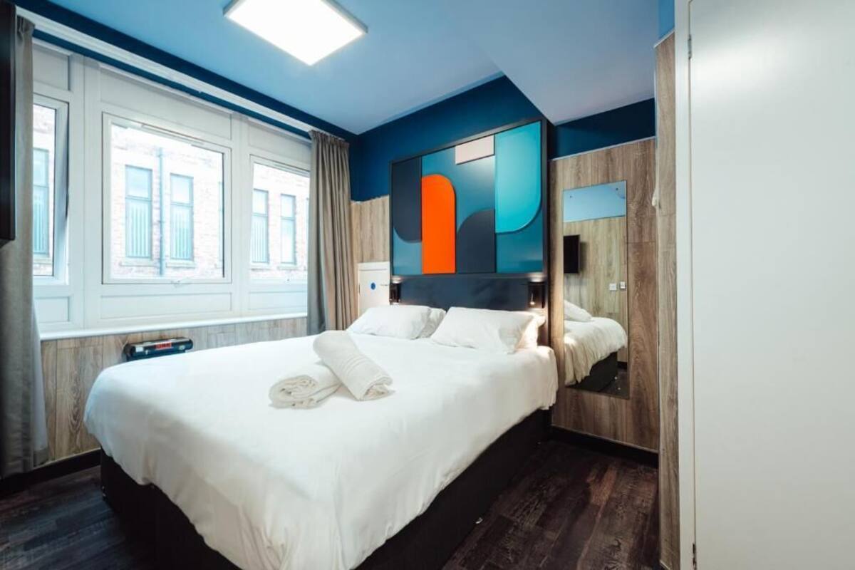 A hotel room with a large bed, a modern abstract painting, a wooden headboard, and a large window.