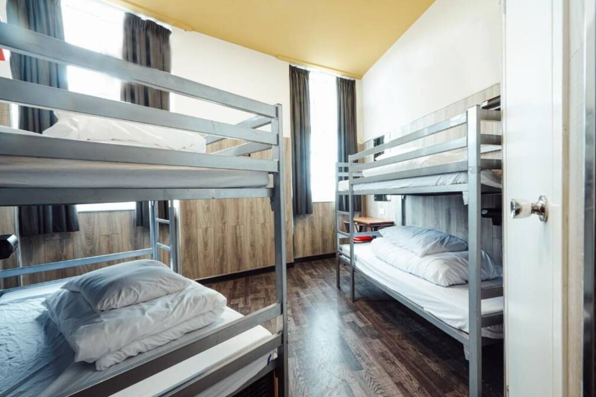 A bunk room with three bunk beds, wooden flooring, and a window with curtains.
