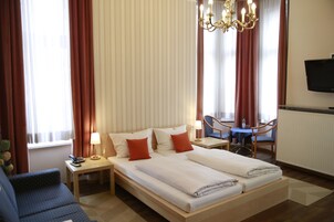 Habitación de hotel con cama doble, mesitas de noche, escritorio, silla, televisor y cortinas.