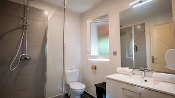 Ein modernes Badezimmer mit einer gläsernen Duschkabine, einer Toilette, einem Waschbecken mit Spiegel und einem Fenster über der Toilette.
