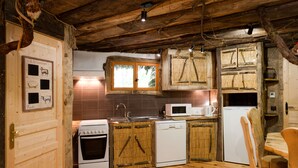 A rustic kitchen with wooden cabinets, a stove, a microwave, and a refrigerator. - Domaine de Dienné (Dienne)
