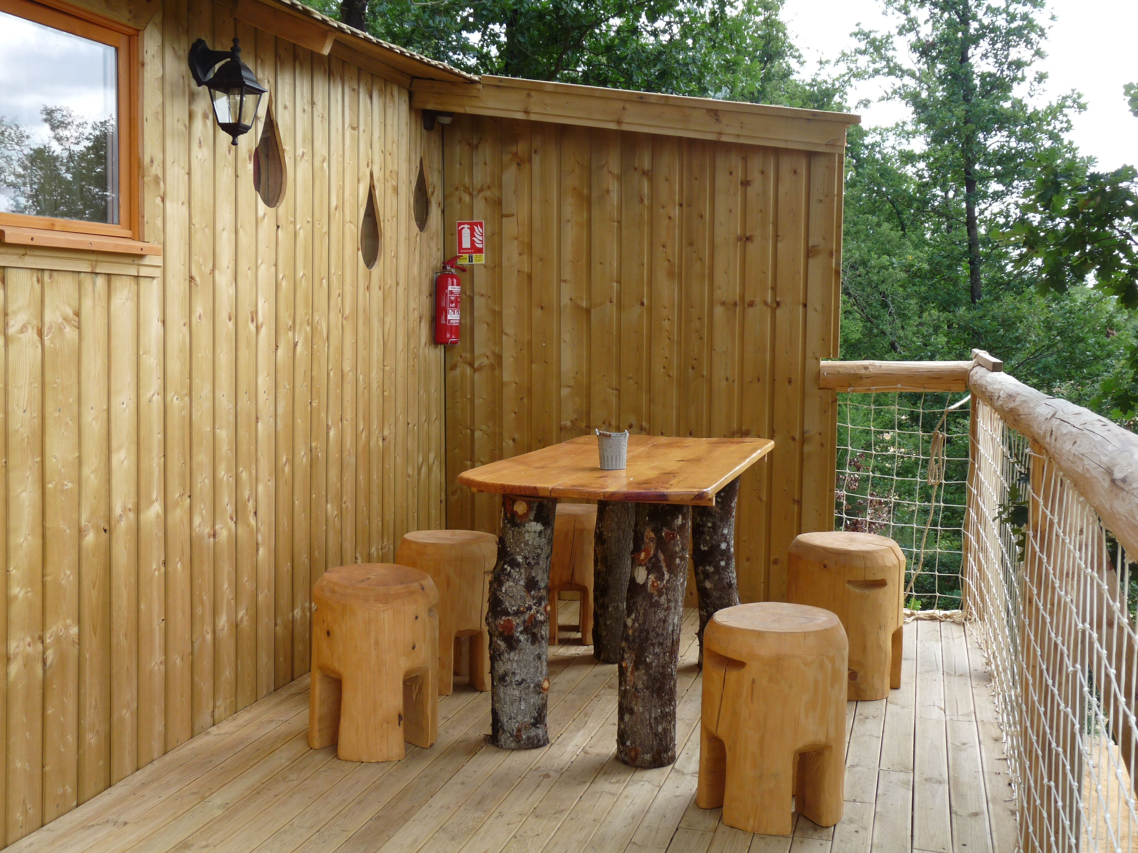 A wooden deck with a table and four stools, surrounded by a wooden fence and trees.