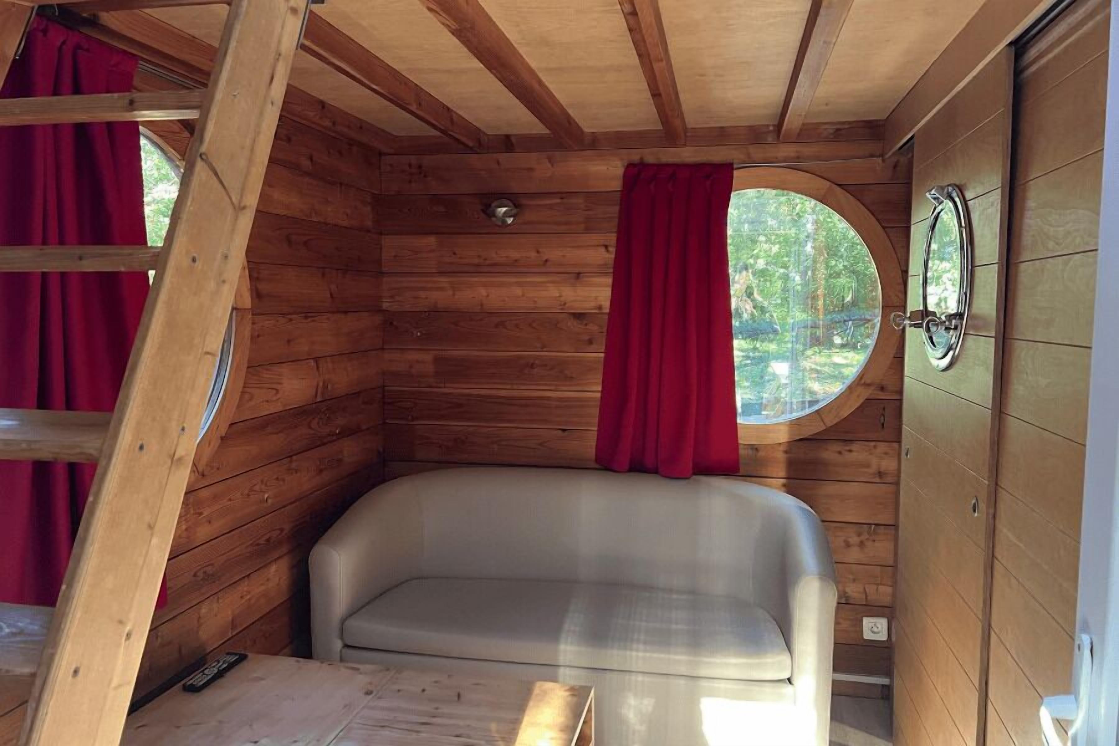 A cozy cabin interior with a wooden interior, a round window, a bathtub, and a red curtain.