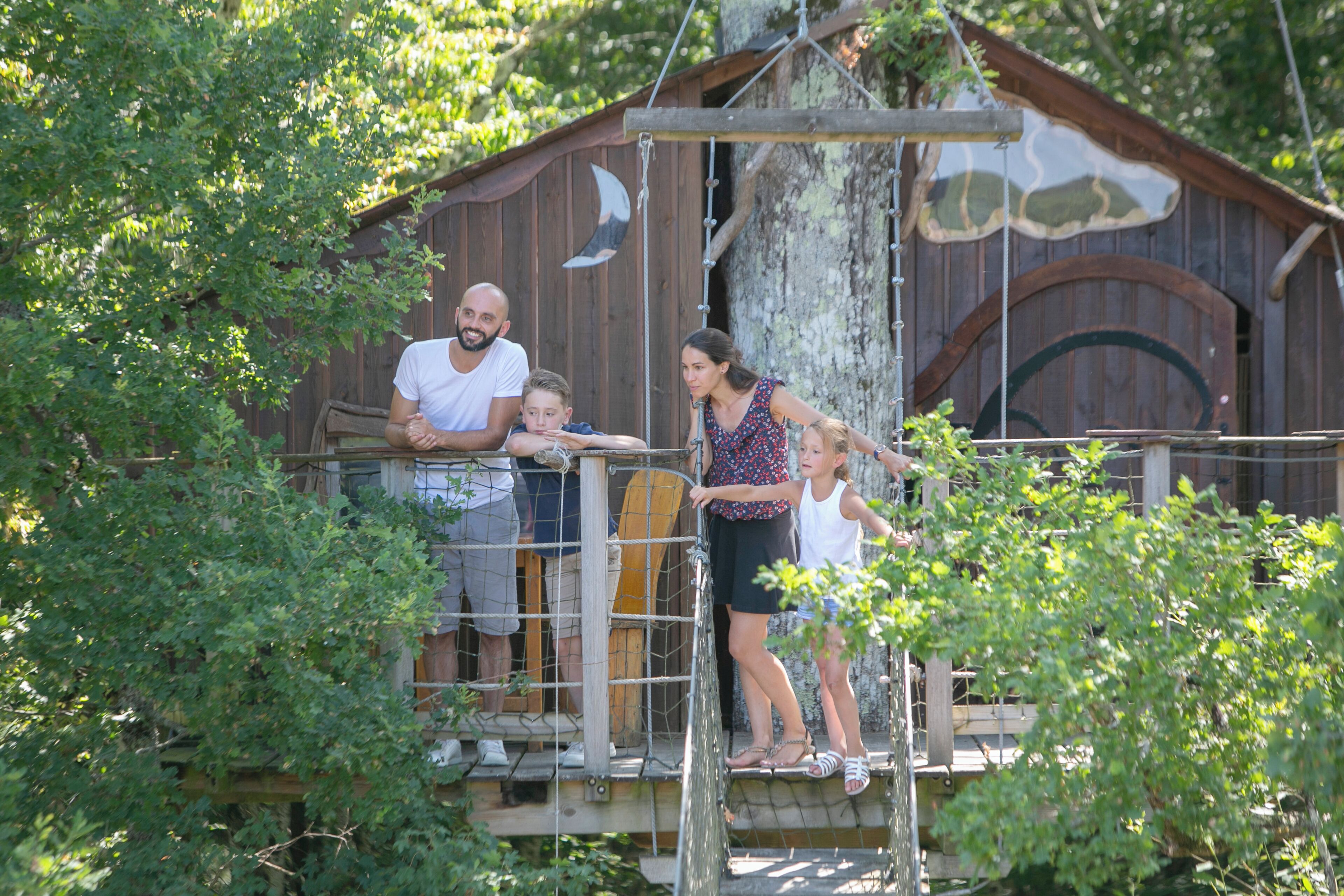 A wooden structure with a rope bridge, surrounded by greenery.
