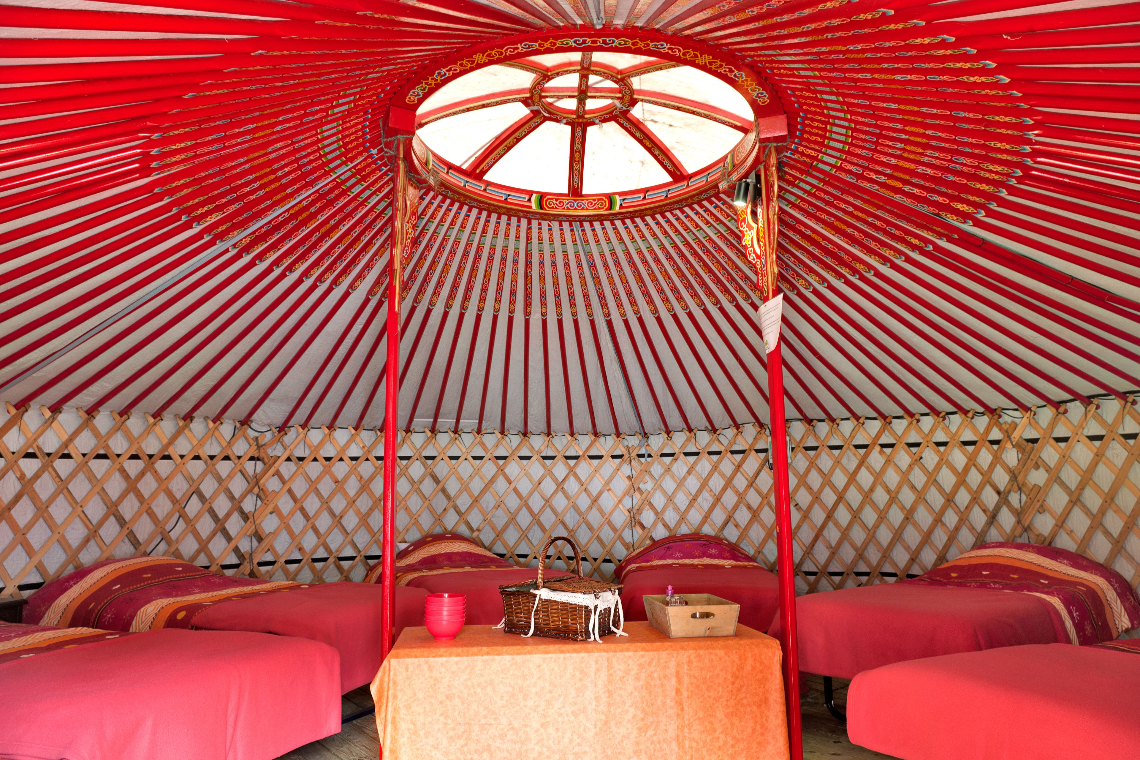 A yurt with four beds, a central table, and a decorative wheel structure.