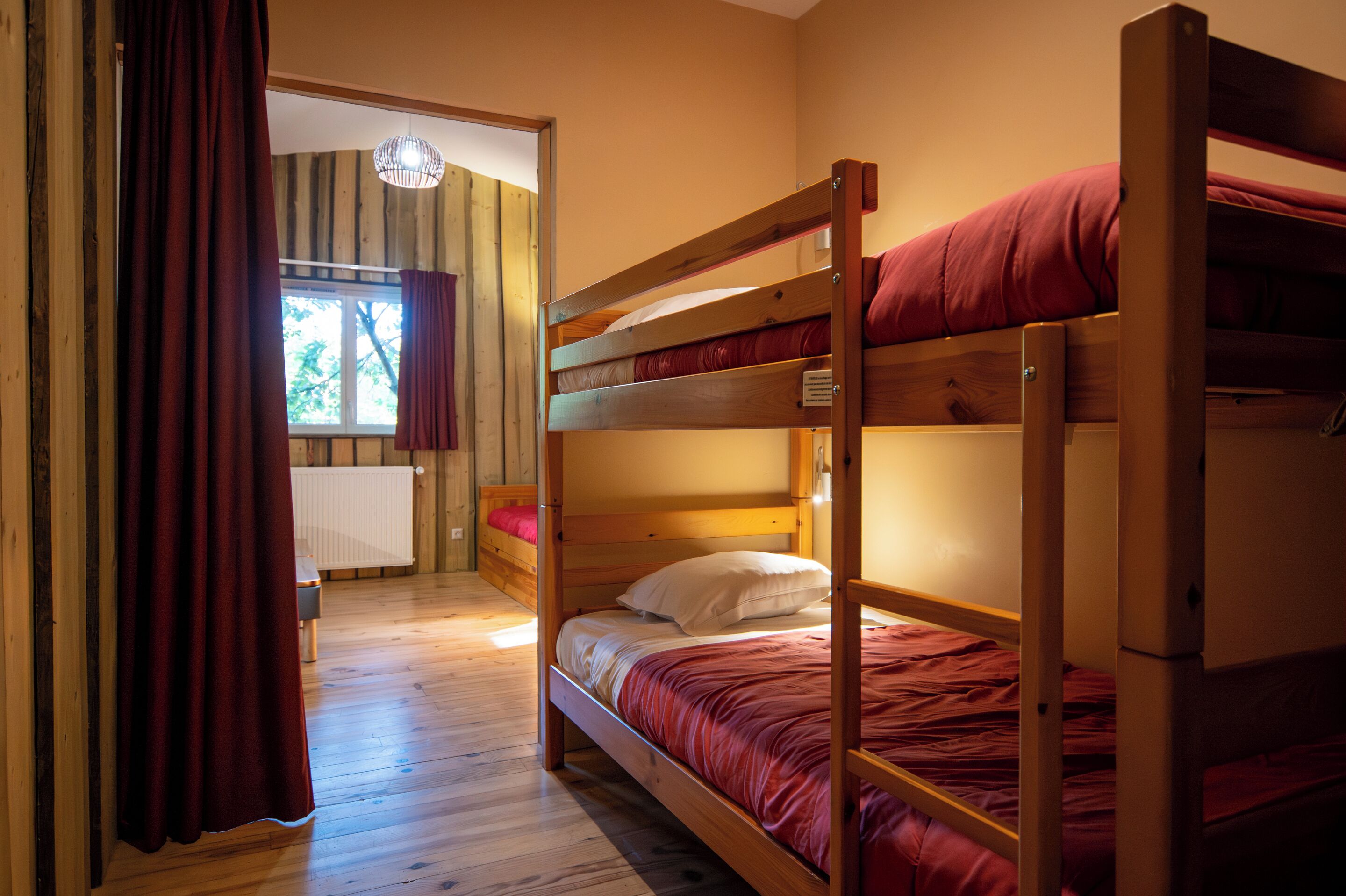 A bunk bed room with a wooden floor, a window with curtains, and a radiator.