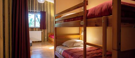 A bunk bed room with a wooden floor, a window with curtains, and a radiator.
