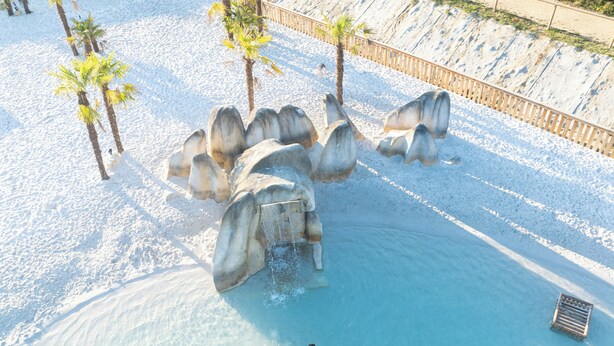 A pool area with clear blue water, surrounded by palm trees and large rock formations. - Domaine de Dienné (Dienne)