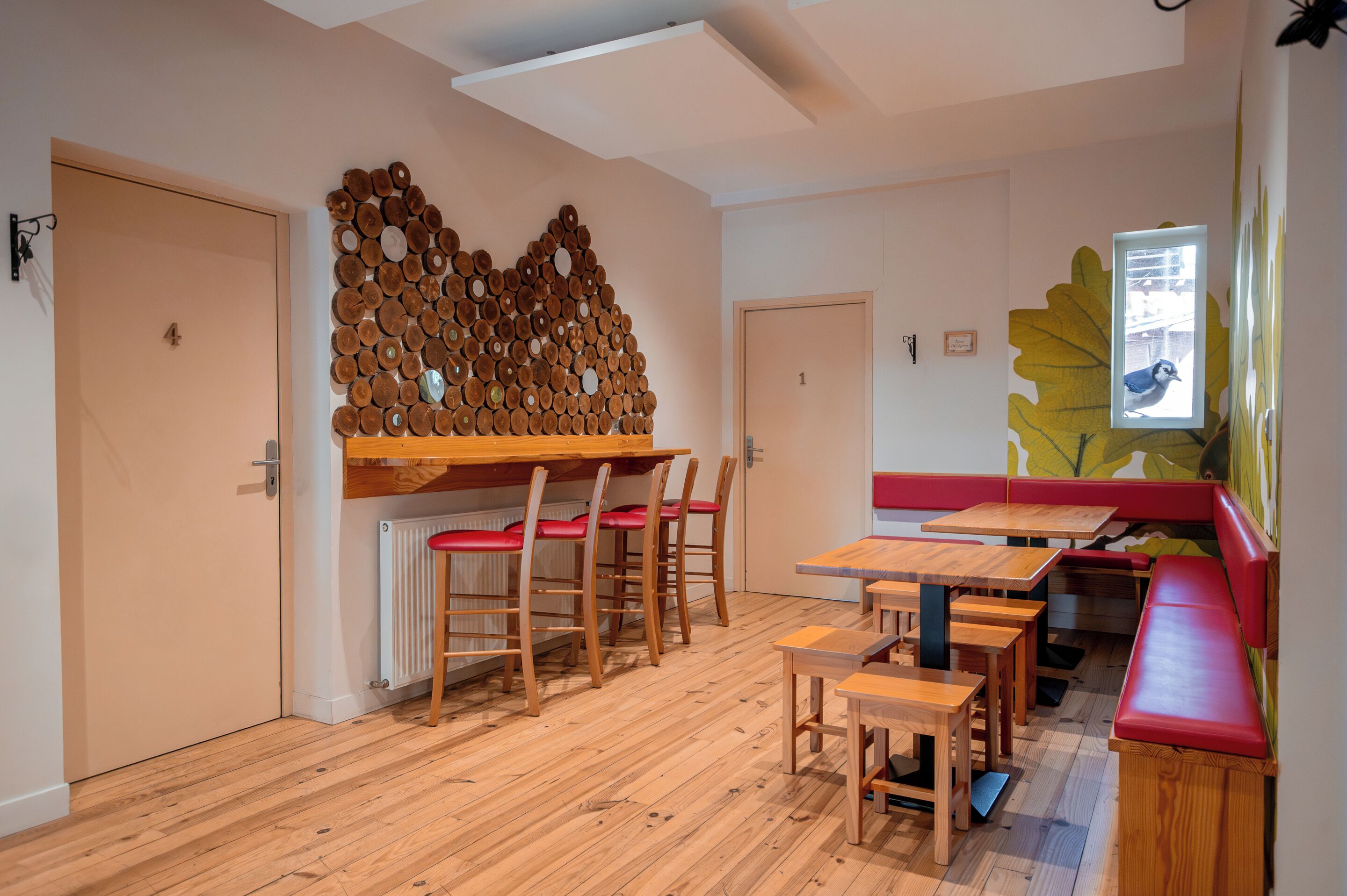 A room with a wooden floor, a wall-mounted wooden art piece, a bench, and a table with chairs.
