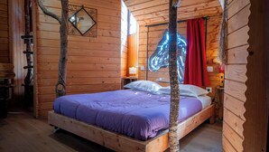 A wooden cabin room with a bed, a nightstand, a lamp, and a mirror on the wall. - Domaine de Dienné (Dienne)