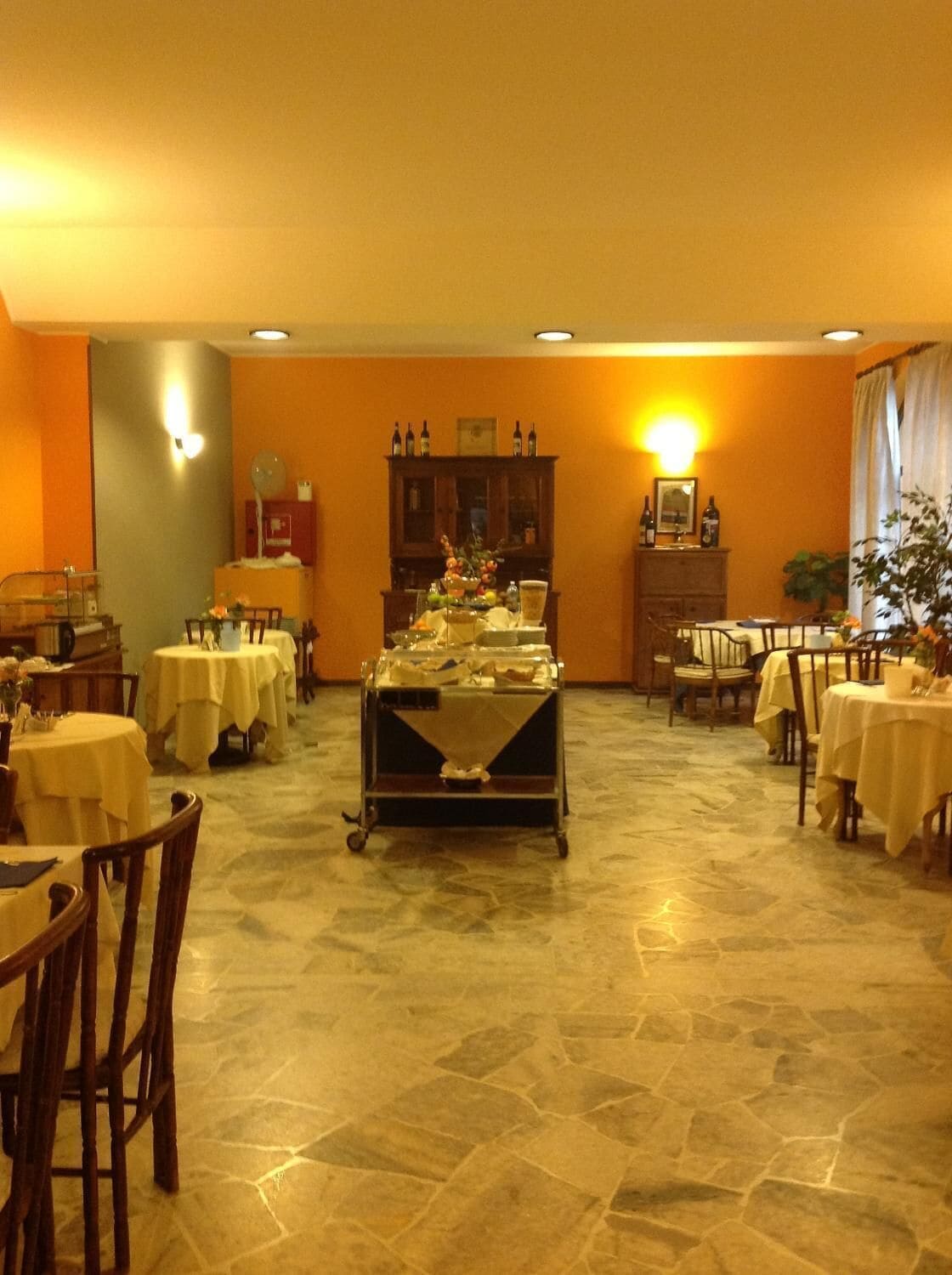 A dining area with multiple tables and chairs, a central serving cart, and a stone-tiled floor.
