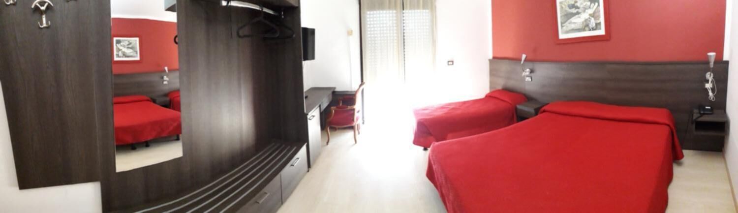 Quarto de hotel com duas camas, um espelho, uma escrivaninha e uma cadeira.