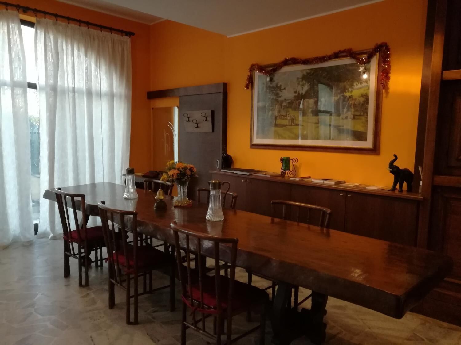A dining area with a long wooden table, chairs, and a decorative mirror on the wall.