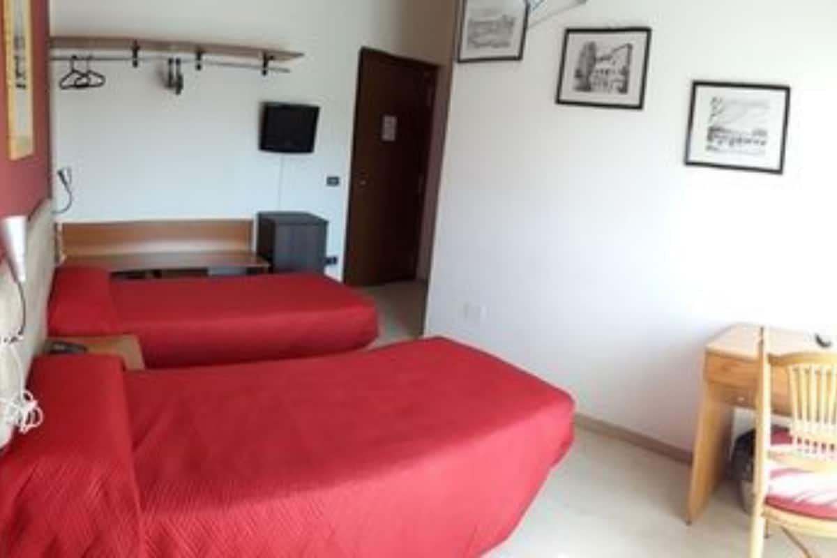 A room with two beds, a chair, a desk, and a television.