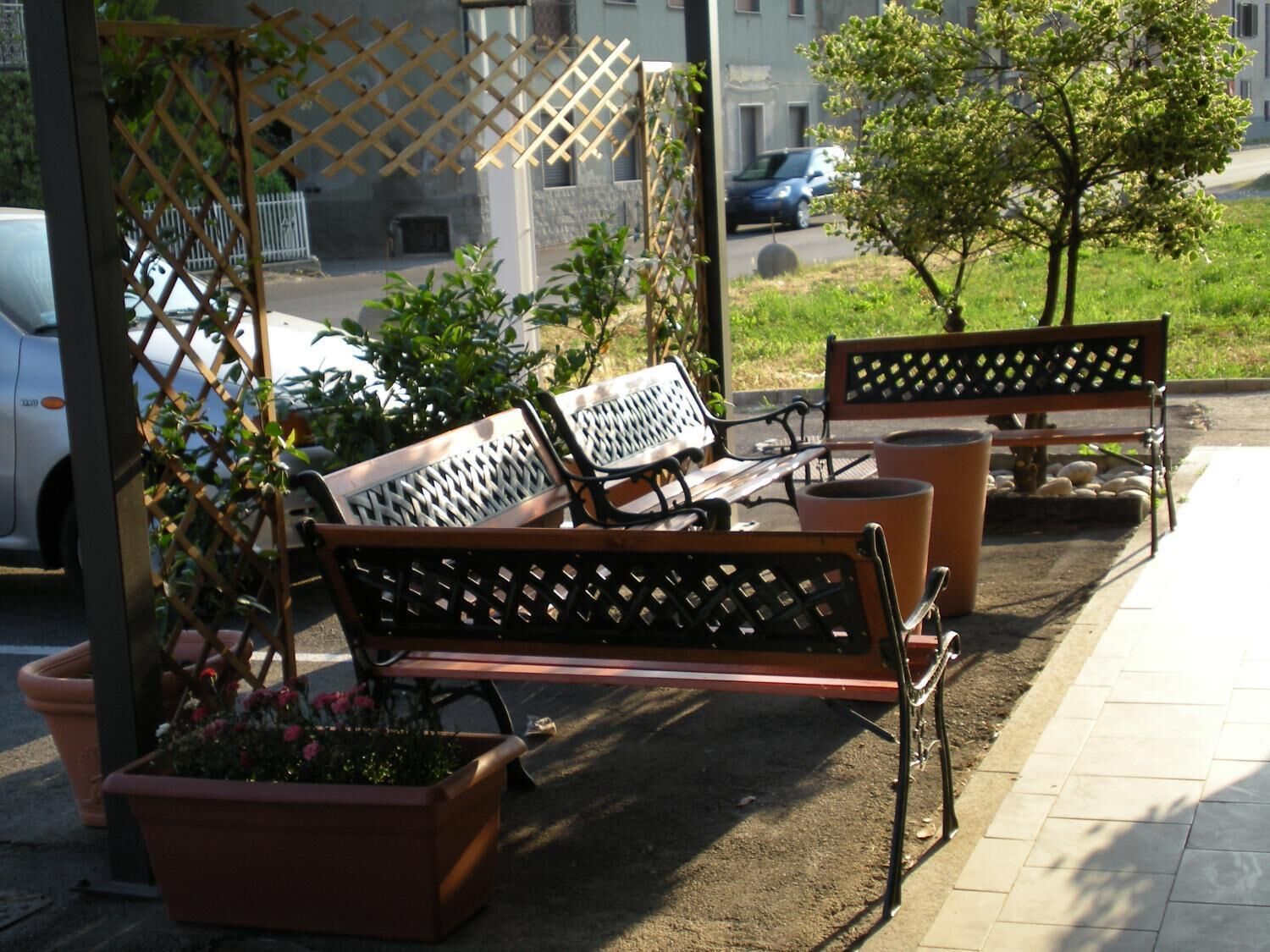 Mobiliario exterior con bancos y jardineras, una valla y un edificio al fondo.