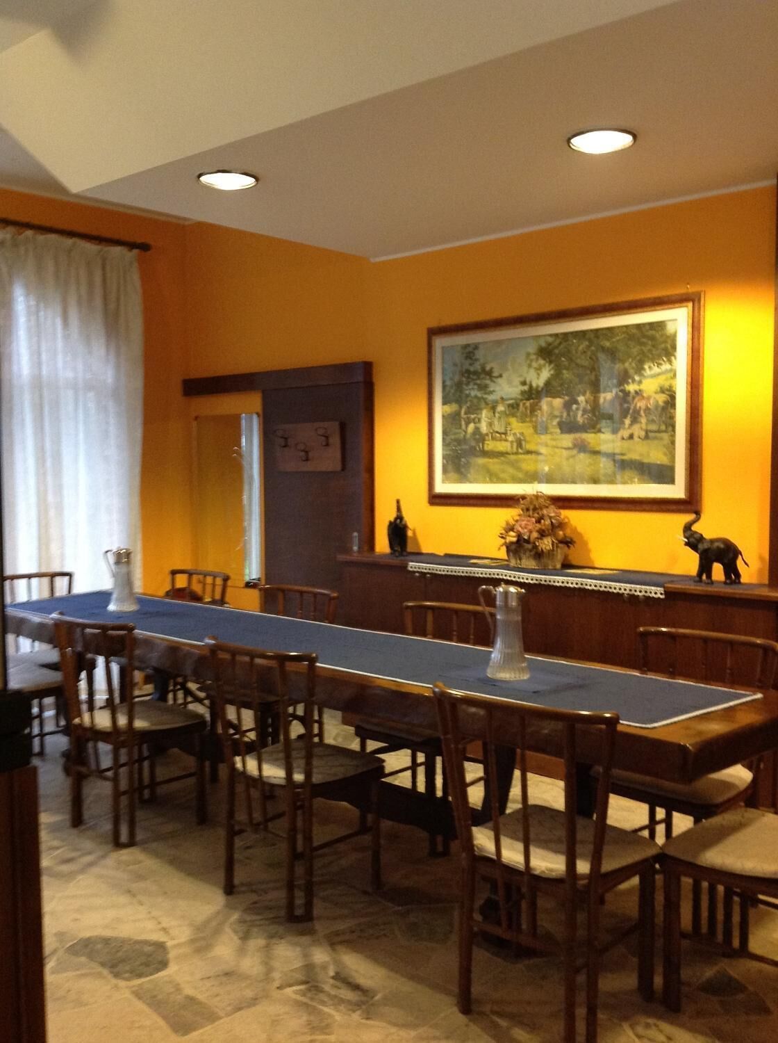 Een eethoek met een lange tafel, houten stoelen en een schilderij aan de muur.